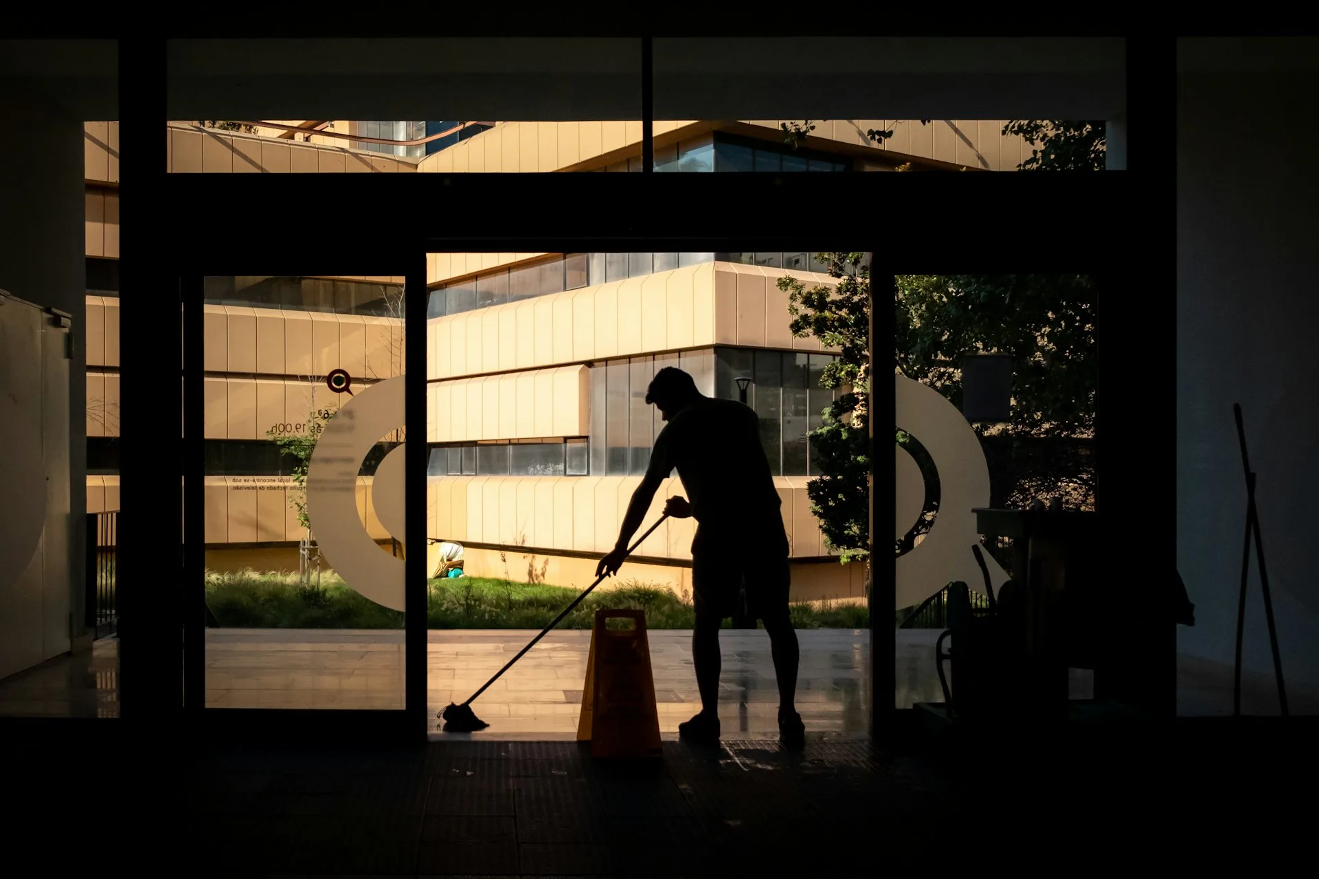 A Travel Clean team member mopping a polished floor at a glass entrance at sunrise
