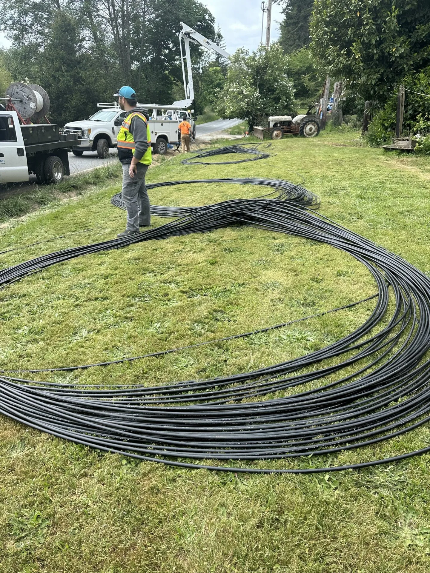 Fiber conduit laid out across a grassy roadside with a bucket truck behind