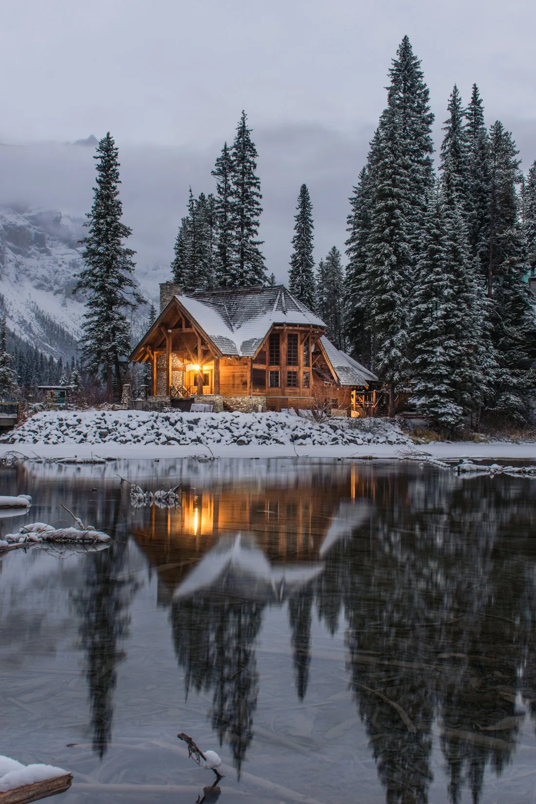 Timber lodge among tall evergreens reflected in still water