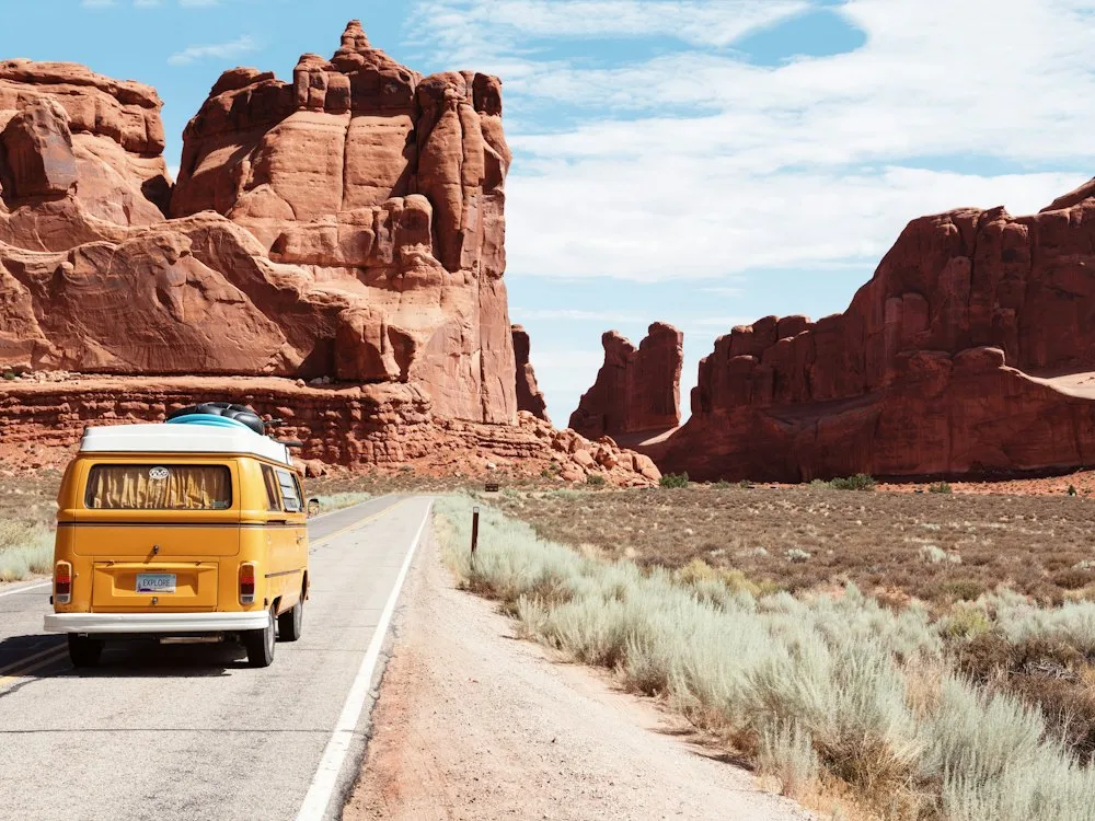 Camper van on a desert highway between red rock formations