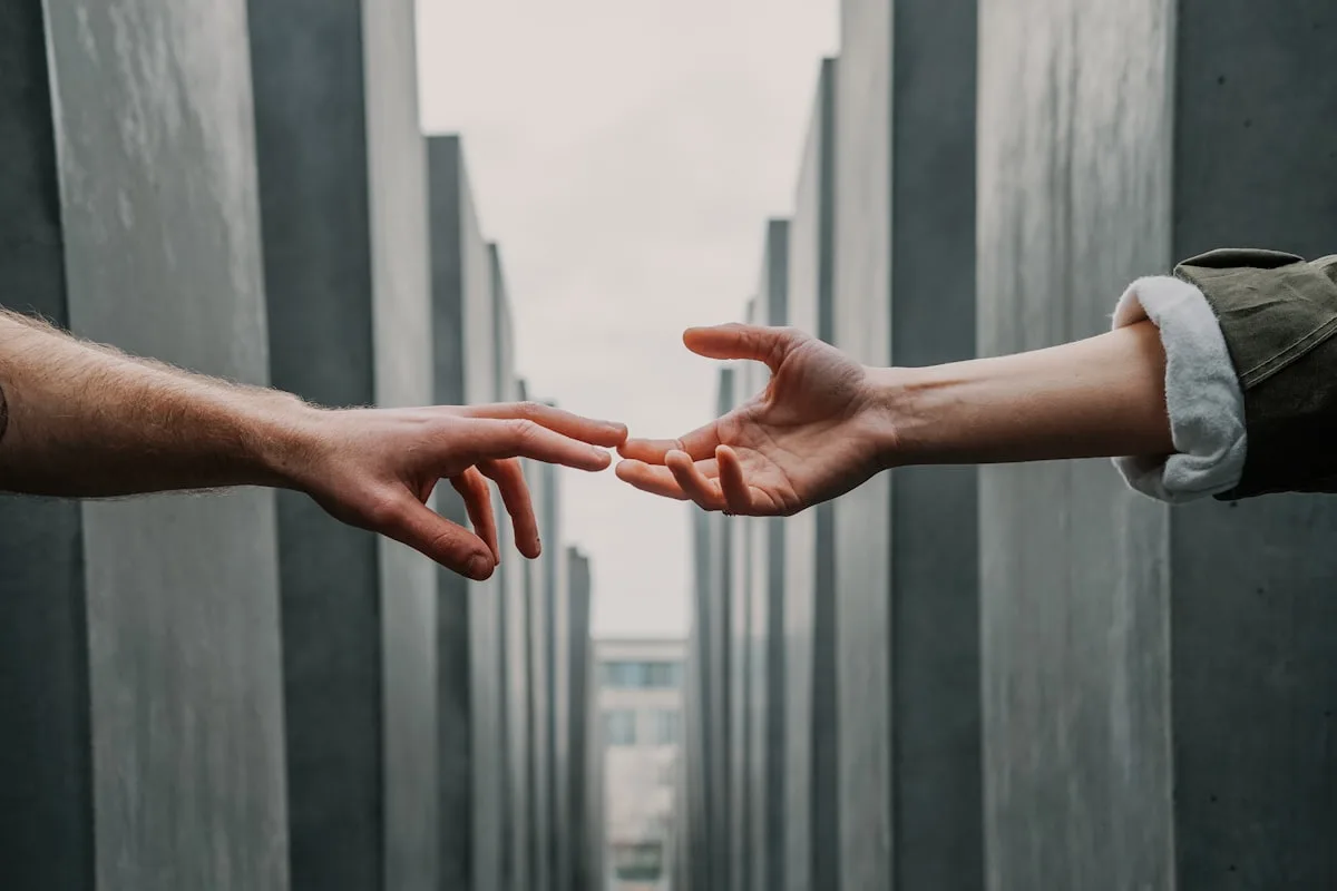 Two people reaching their hands toward each other between tall concrete pillars