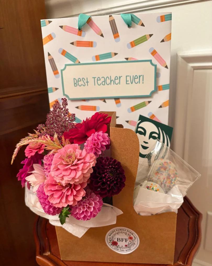 A kraft carrier of pink and burgundy dahlias and zinnias with a Starbucks gift card and sprinkled chocolate-covered Oreos, in front of a Best Teacher Ever gift bag