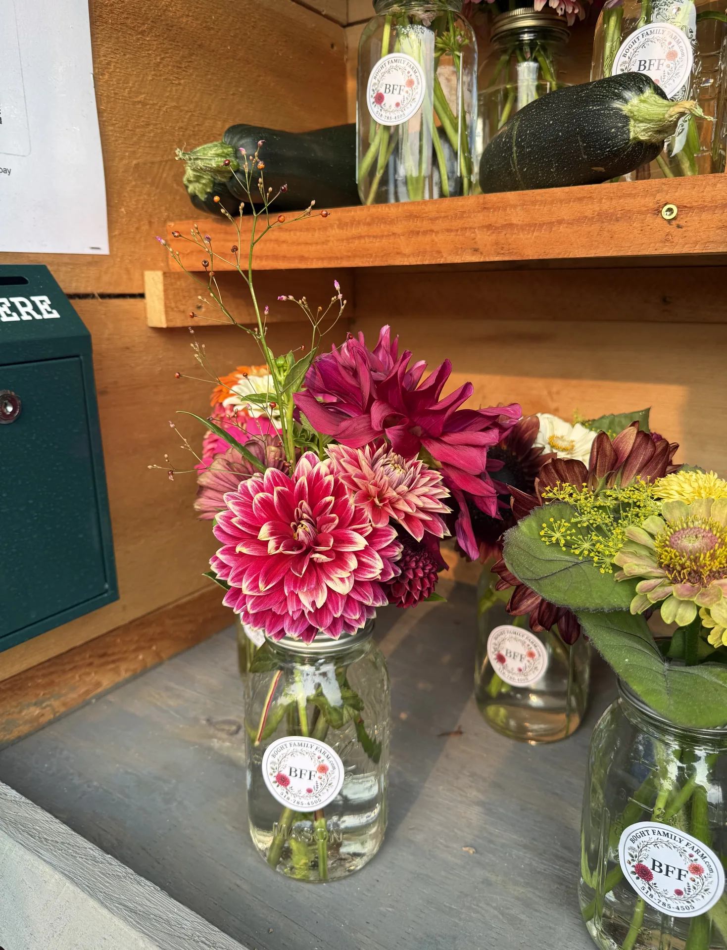 The farm stand shelf: labelled jars of flowers, garden zucchini, and the honor box