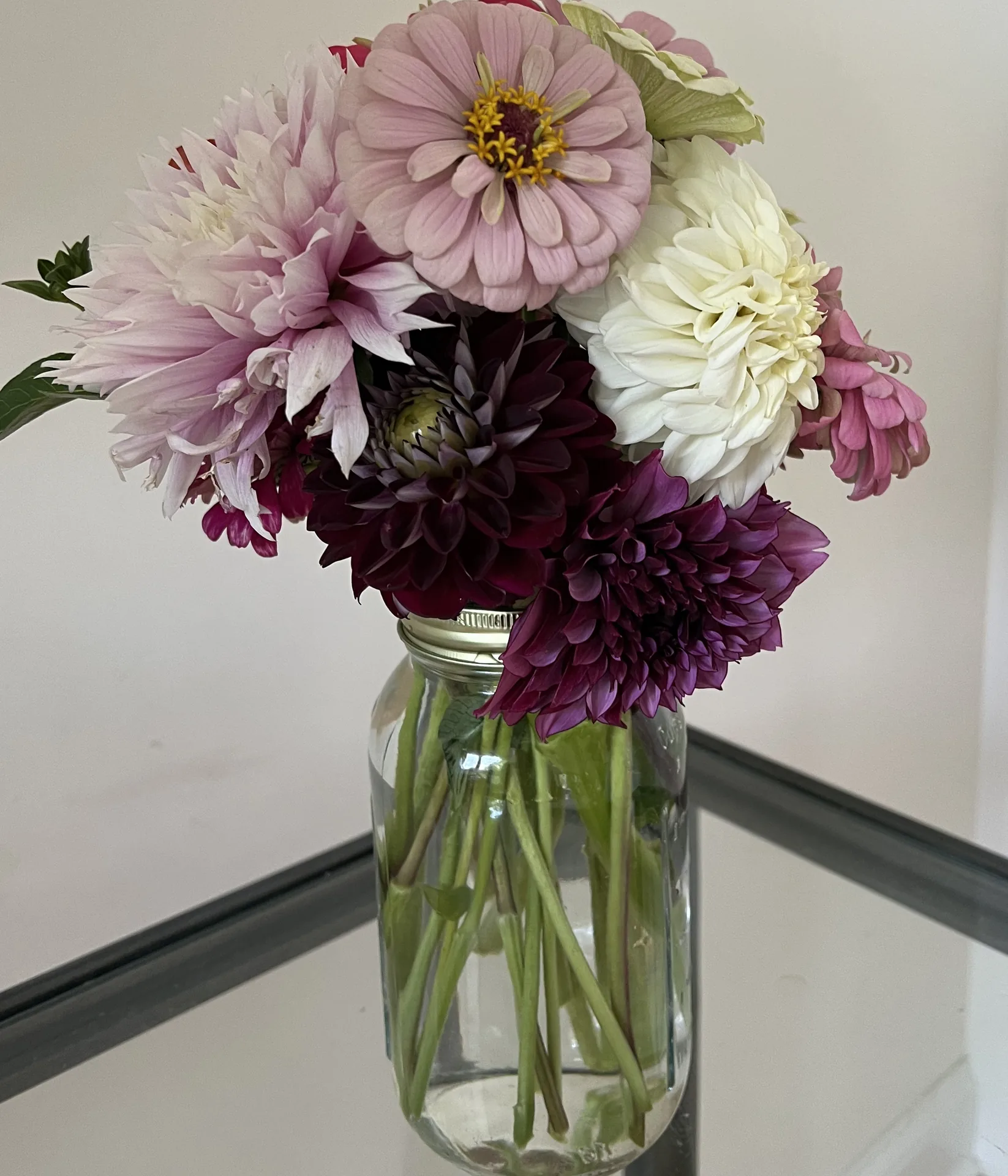A canning jar of dusty pink and burgundy dahlias on a glass table