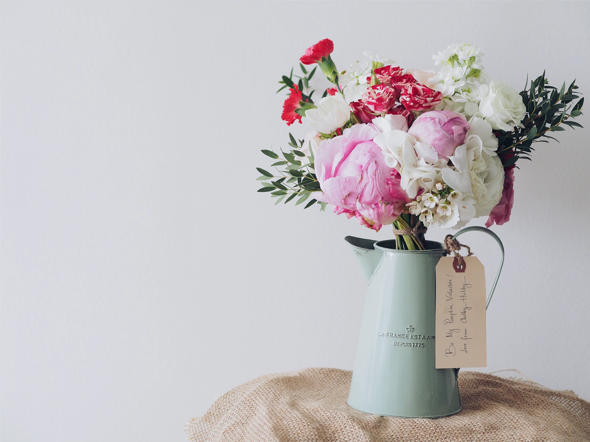 A pitcher of peonies and garden roses with a hand-written tag