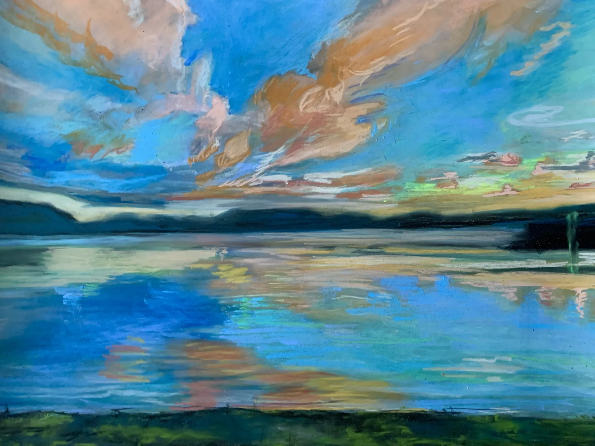 Pastel of an apricot and salmon cloudbank torn across blue sky, reflected in still water below a dark treeline