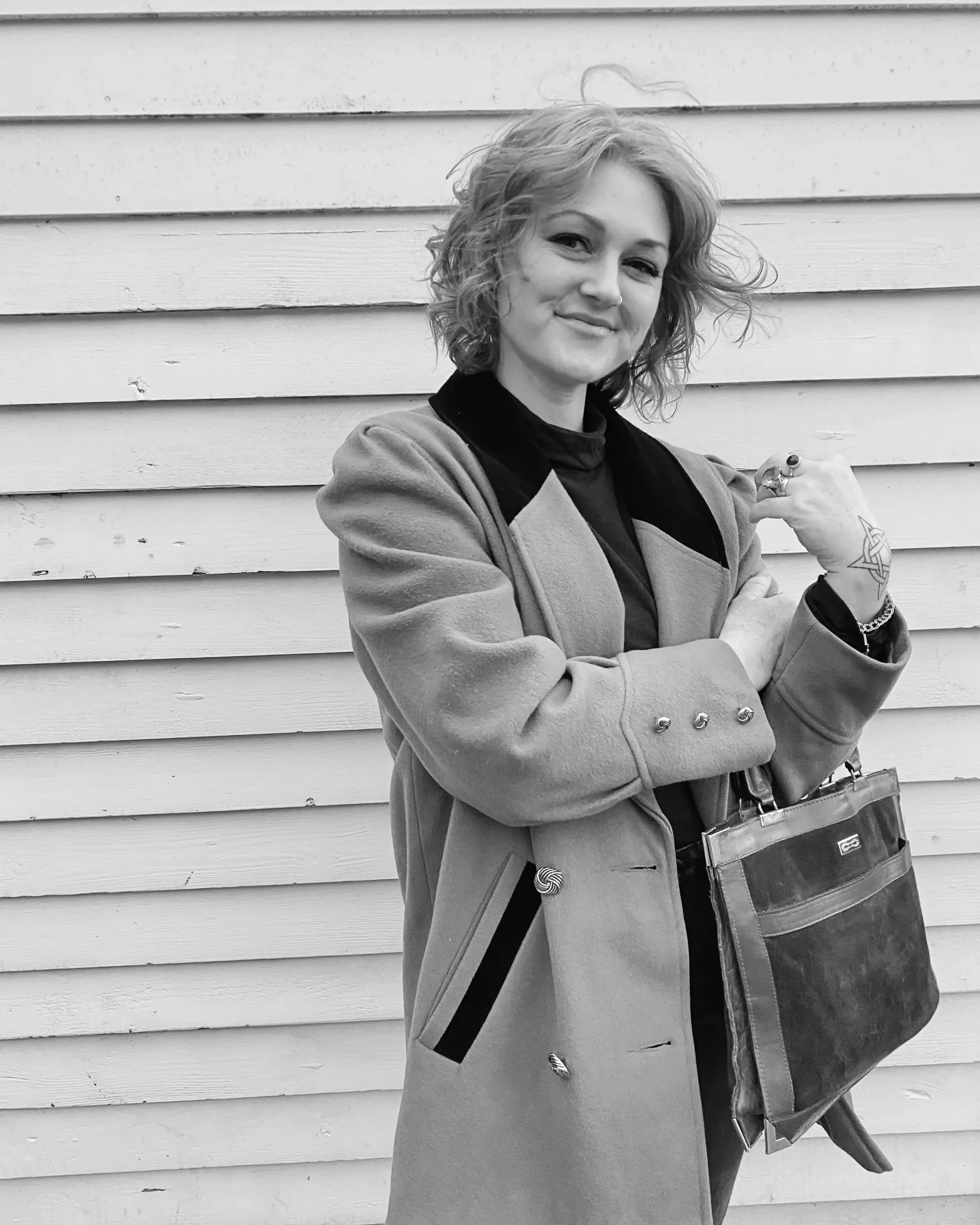 Black and white portrait of Whitney Page in a wool coat against a clapboard wall