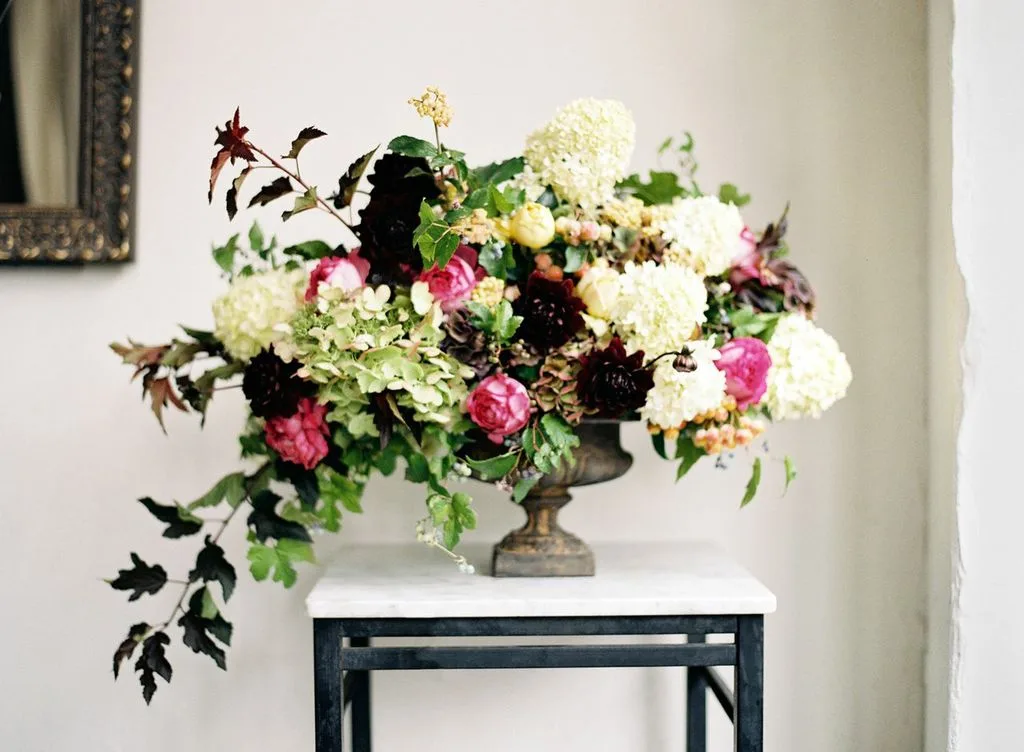 A large urn arrangement of white hydrangea, pink peonies and dark dahlias on a marble table