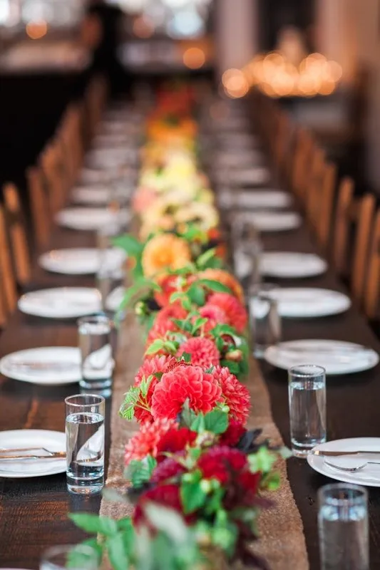 A long runner of red and orange dahlias down the center of a set dinner table
