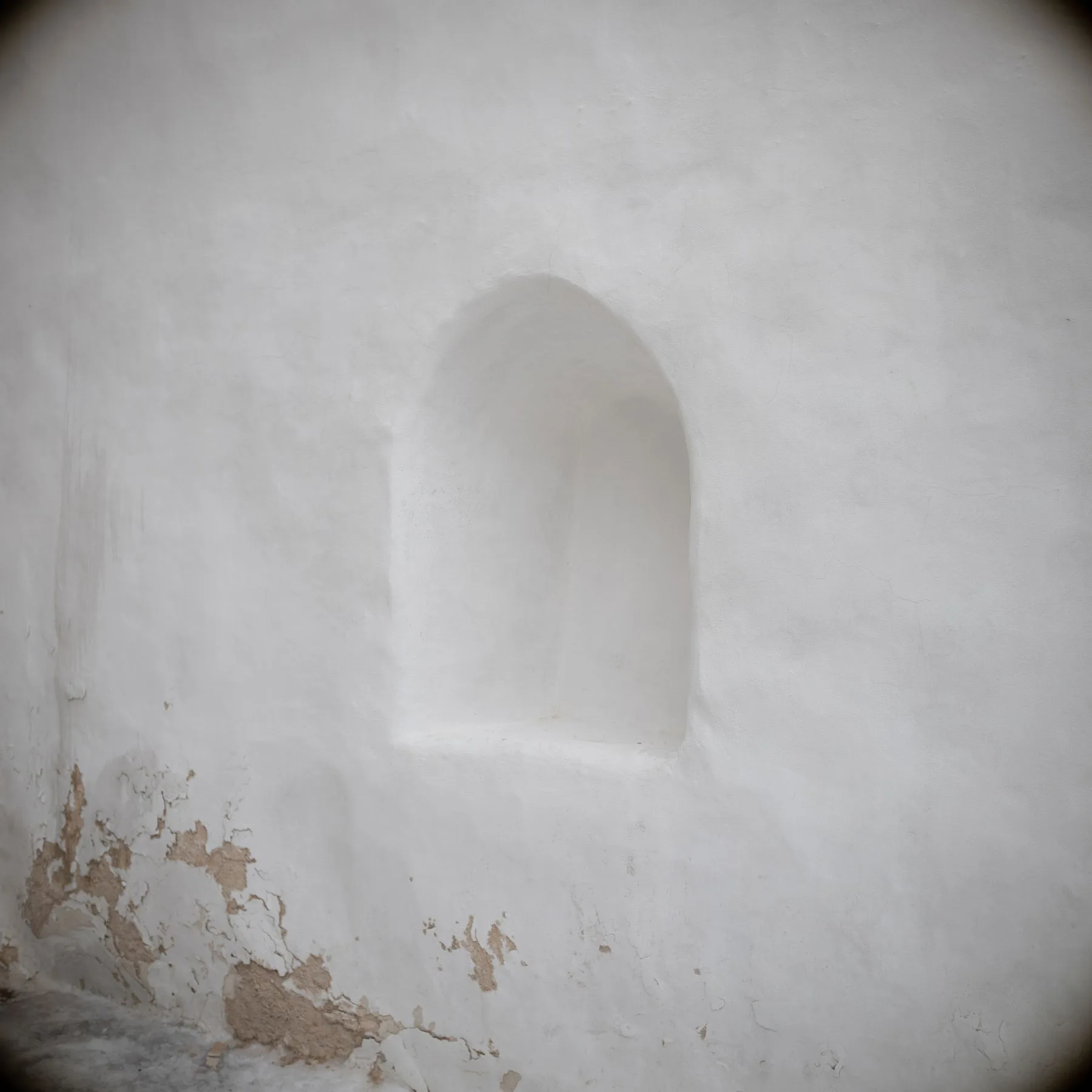 A softly trowelled lime plaster wall with an arched niche and a weathered patch at the base