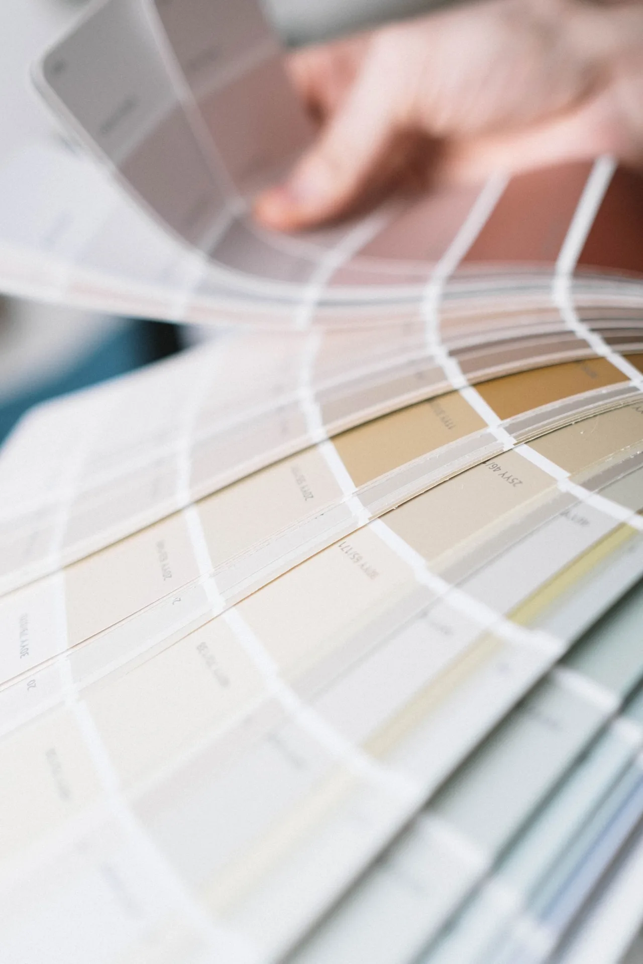 A hand turning the pages of a natural paint fan deck in soft chalky neutrals