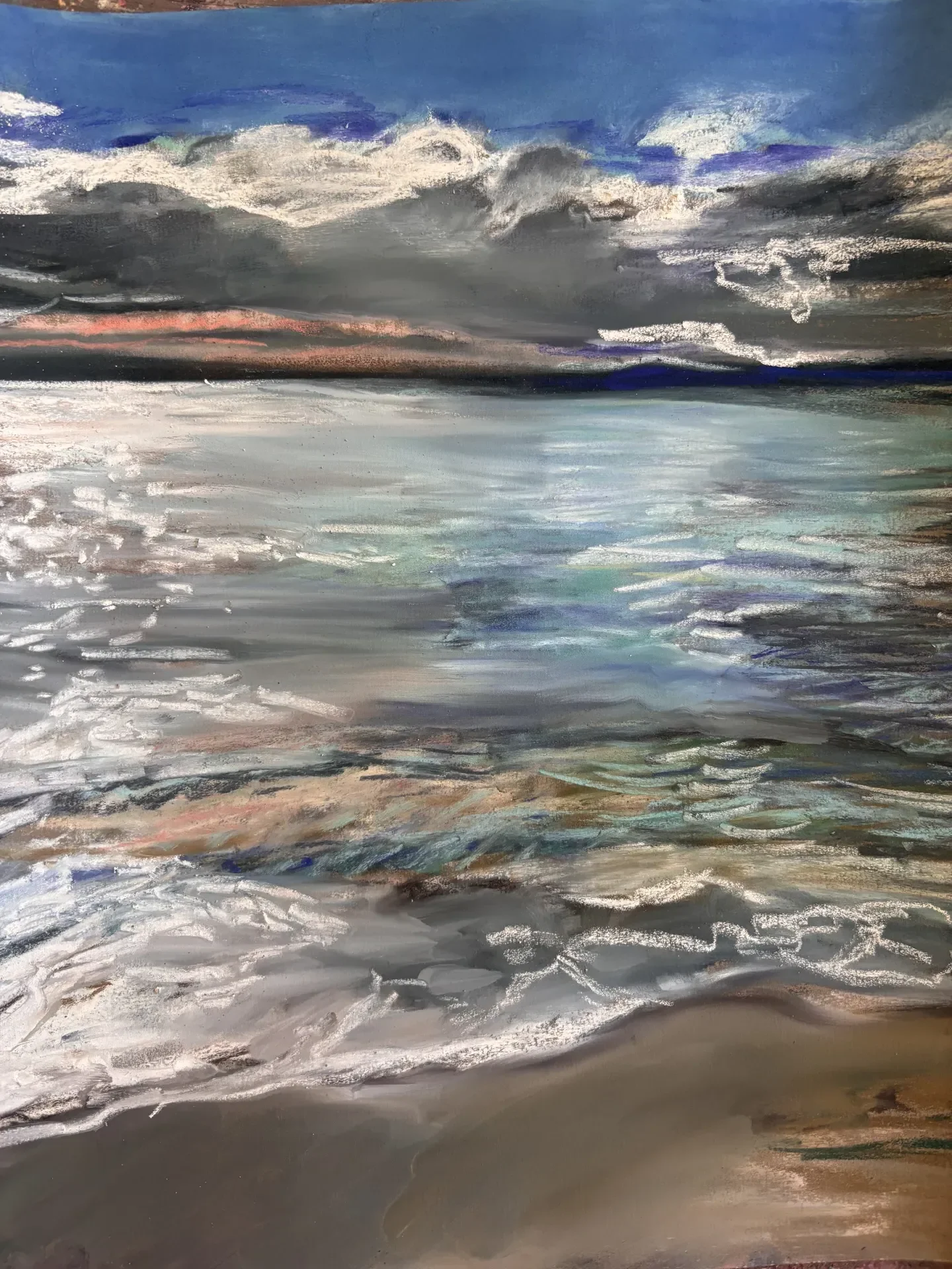 Pastel of a shoreline under weather: blue sky, a dark bank of cloud, pale water breaking over wet sand