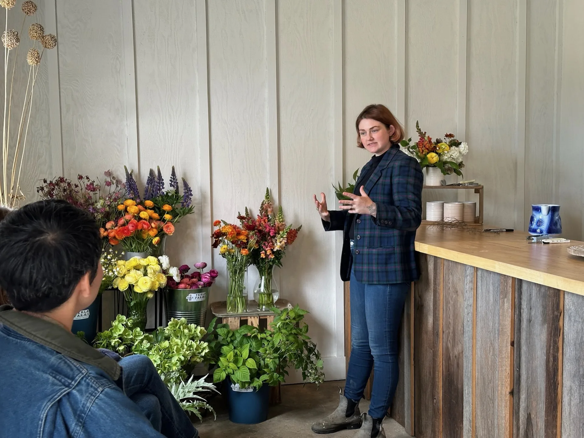 Whitney Page talking with a student in the design studio at Tekla Farms, beside buckets of ranunculus, lupine, snapdragons and hydrangea cut that morning