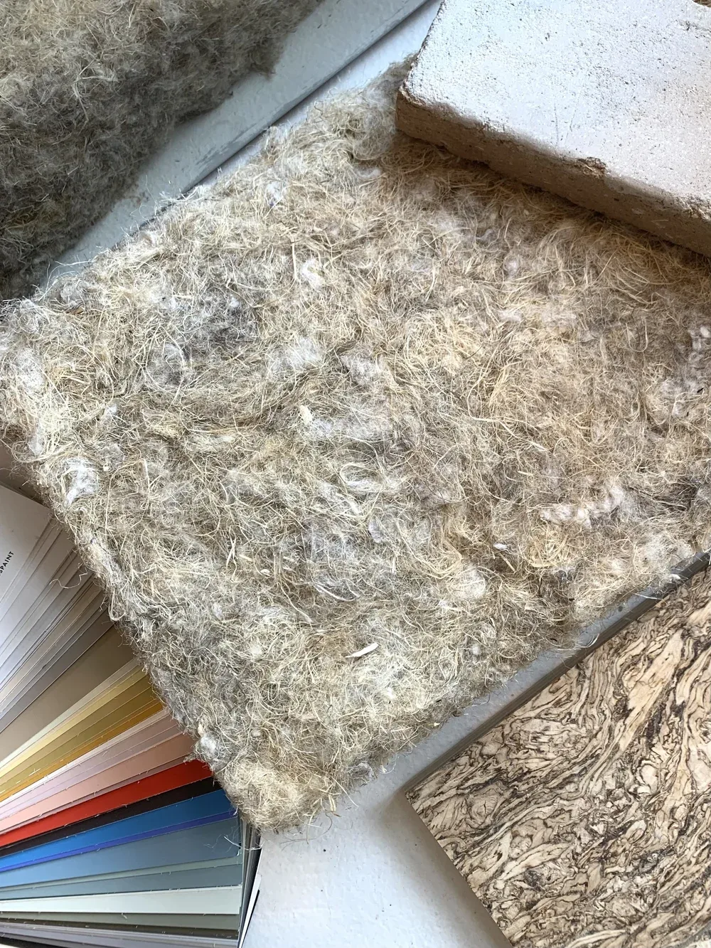 Sheep wool insulation, a hemp-lime block and a cork sheet beside a natural paint sample book