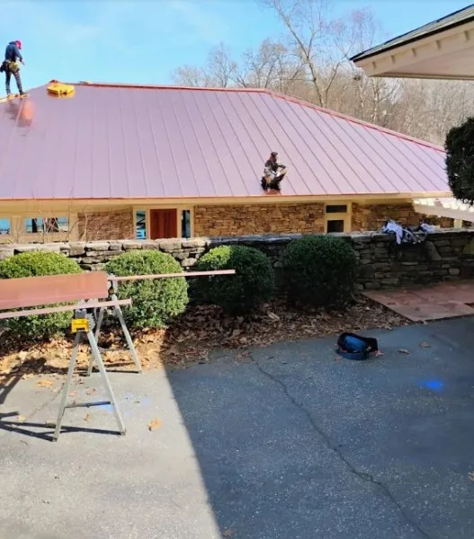 Crew installing a copper-colored metal roof on a stone home