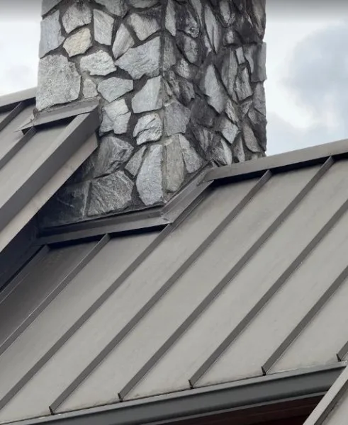 Standing seam metal roof with flashing around a stone chimney