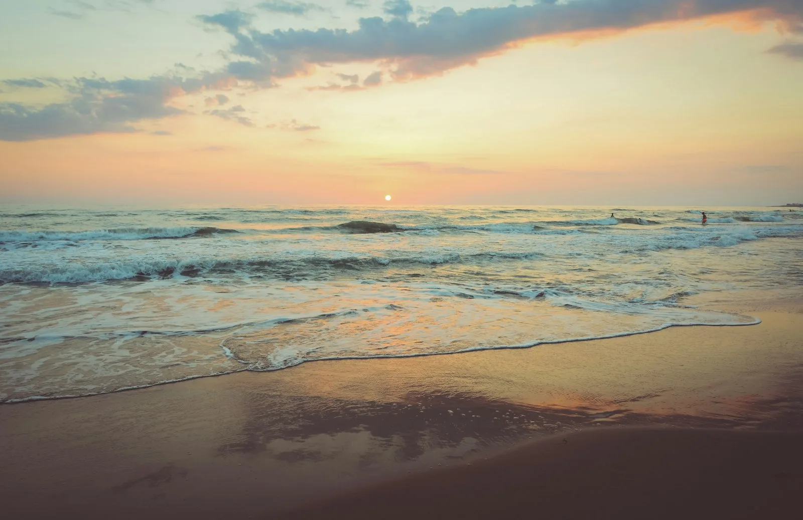 The sun setting over the sea with gentle surf along the shore
