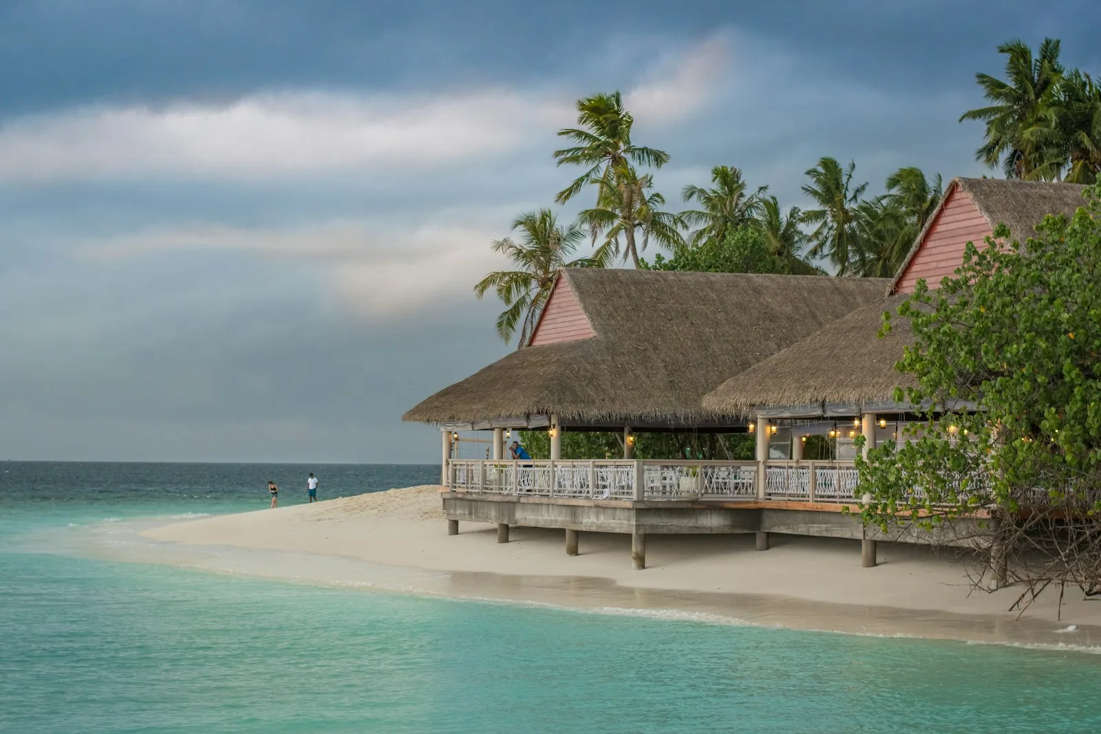 A thatched-roof beach house restaurant on stilts above white sand and turquoise water