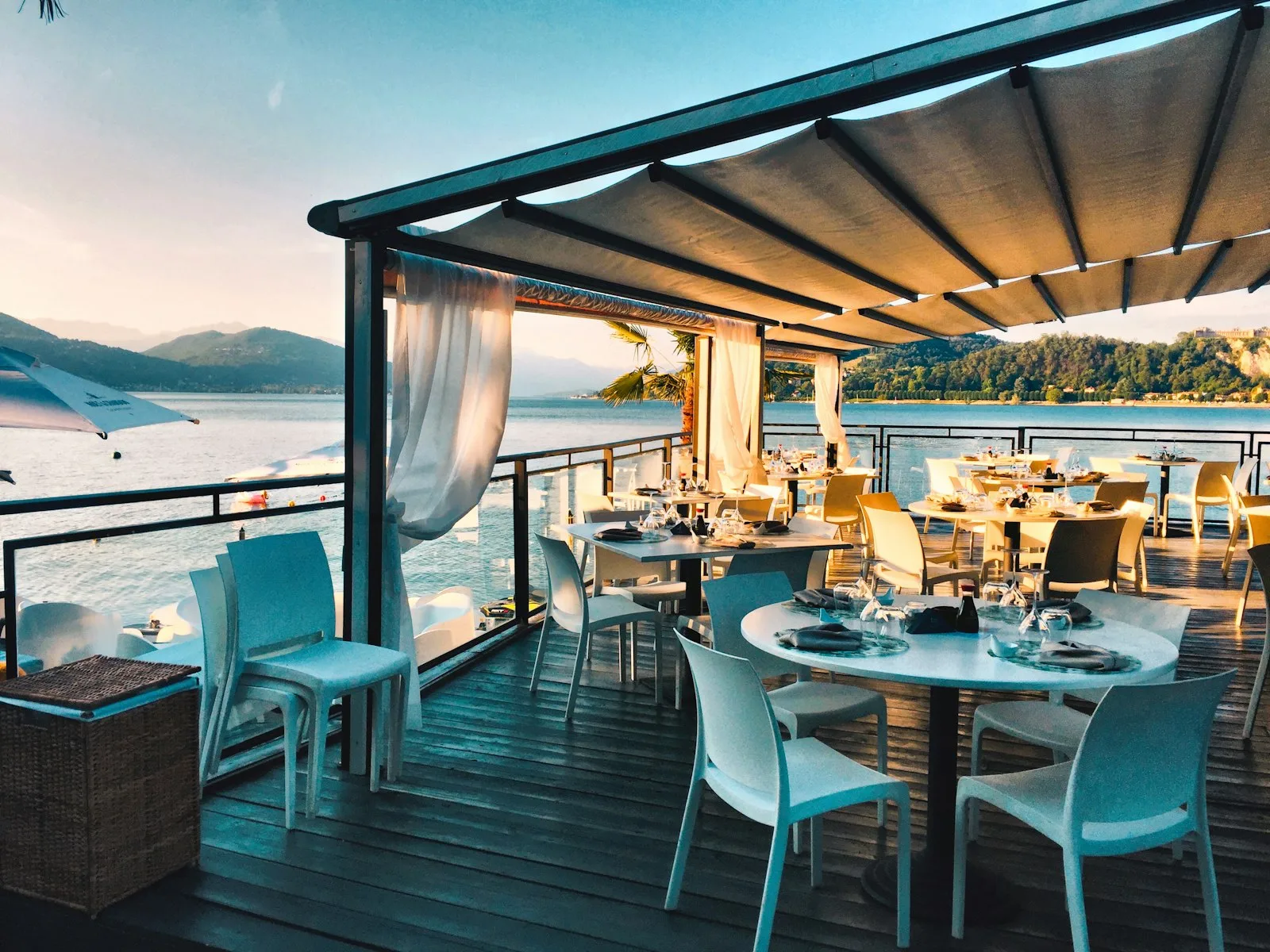 An open-air dining terrace with white tables overlooking the water at sunset