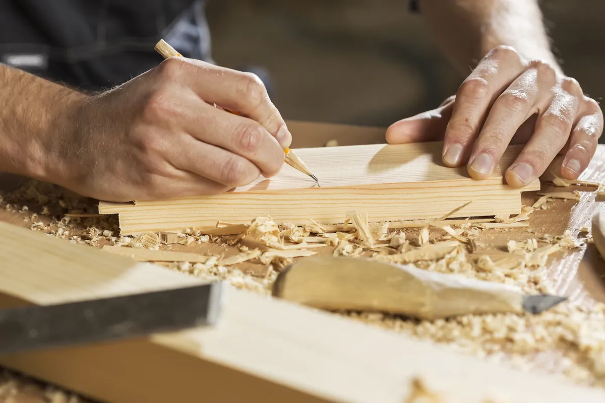 Hands marking a cut line on a board with a pencil and square