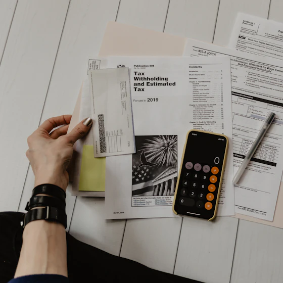Tax forms, a calculator and a pen laid out on a desk