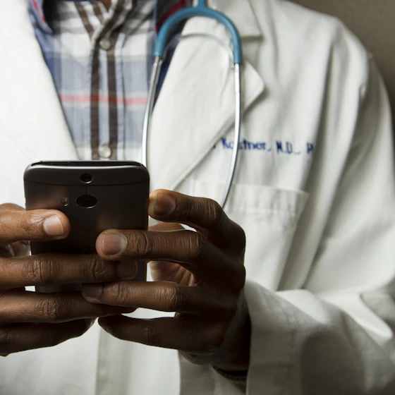 A clinician in a white coat using a smartphone