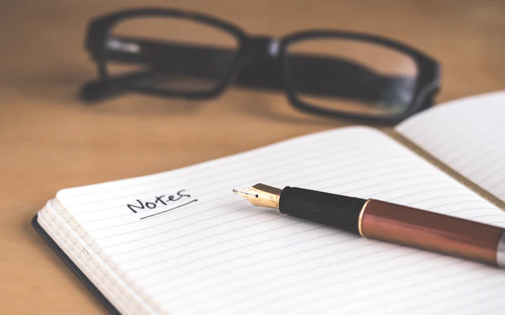 An open notebook headed Notes with a fountain pen and reading glasses