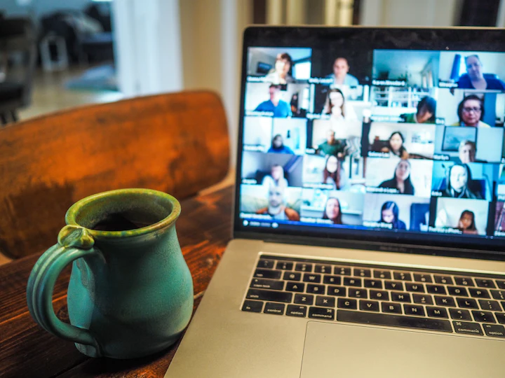 A laptop on a kitchen table showing a grid of people on a video call