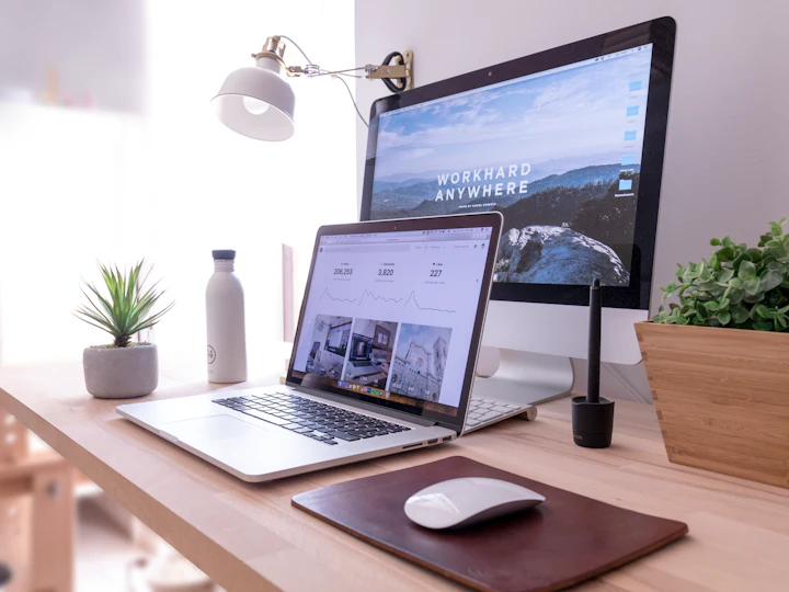 A laptop and monitor on a wooden desk showing a website design
