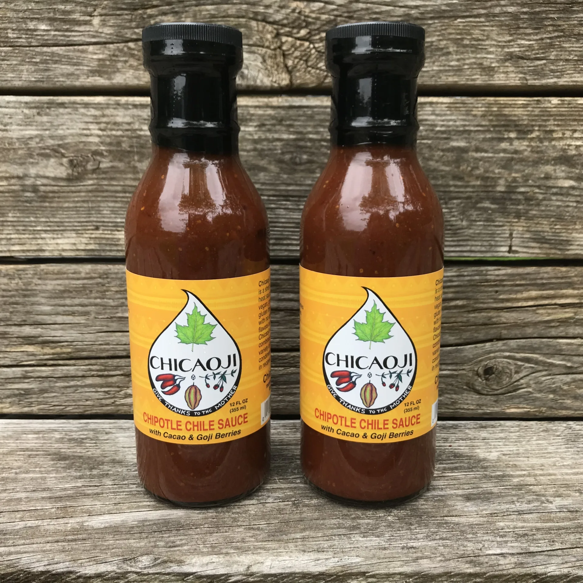 Two bottles of Chicaoji chipotle chile sauce with cacao and goji berries on a rustic wood table