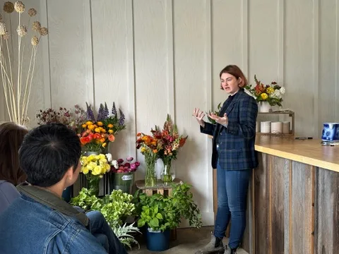 A designer teaching a floral workshop, with students at a table of fresh flowers and vases