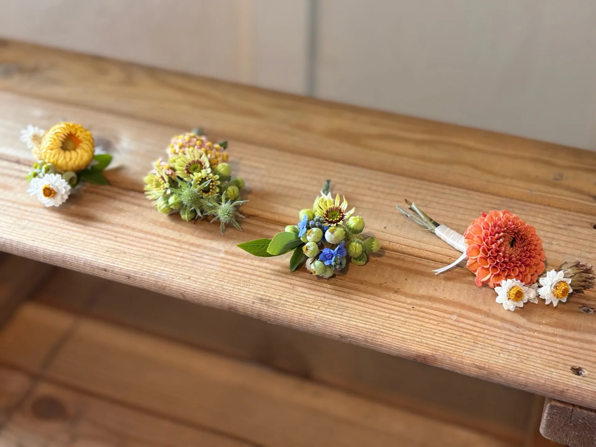 Collection of delicate wedding boutonnieres and small floral arrangements on a wooden surface, showcasing detailed floral design work