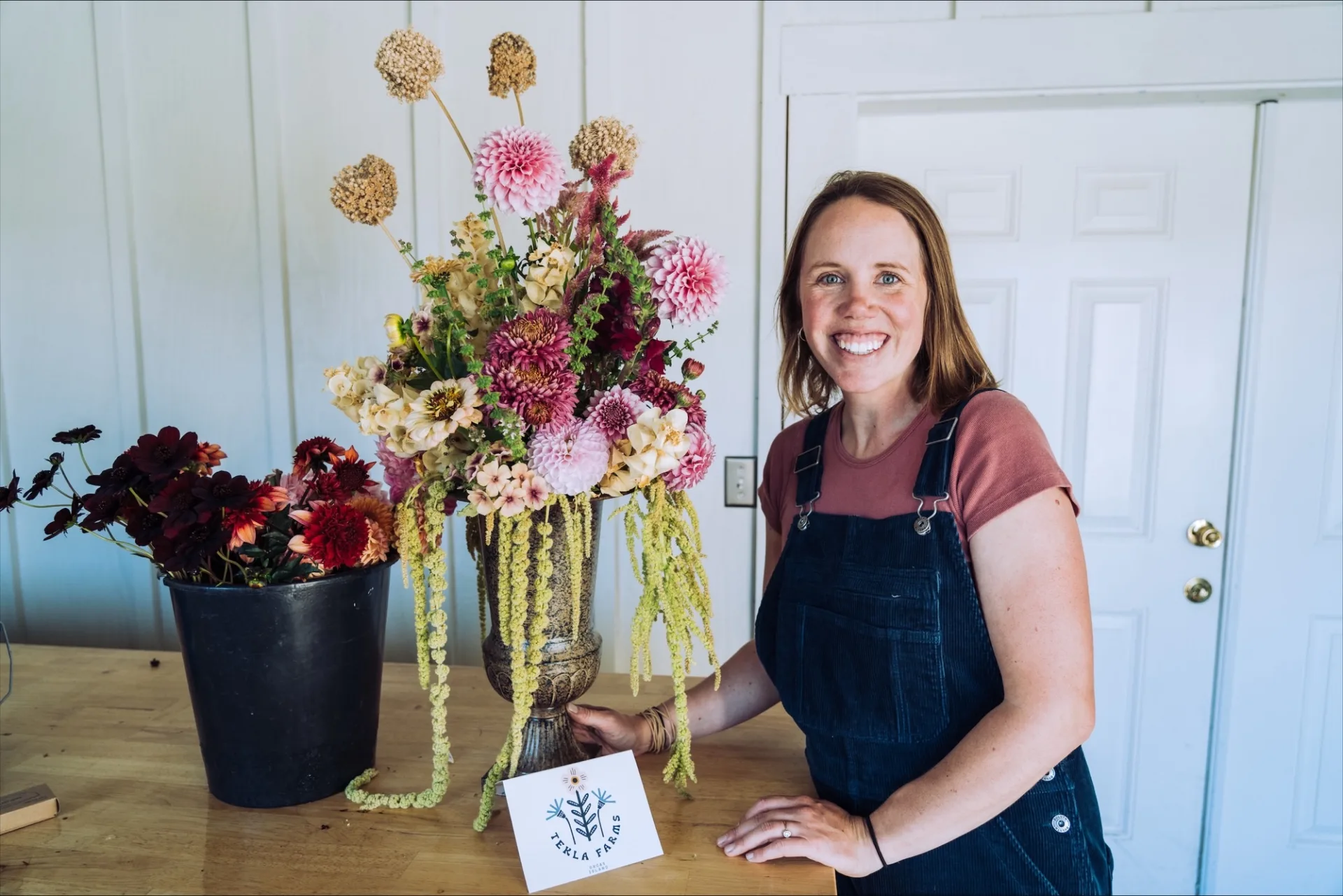 Laura smiling beside a large arrangement of dahlias, amaranthus and dried alliums