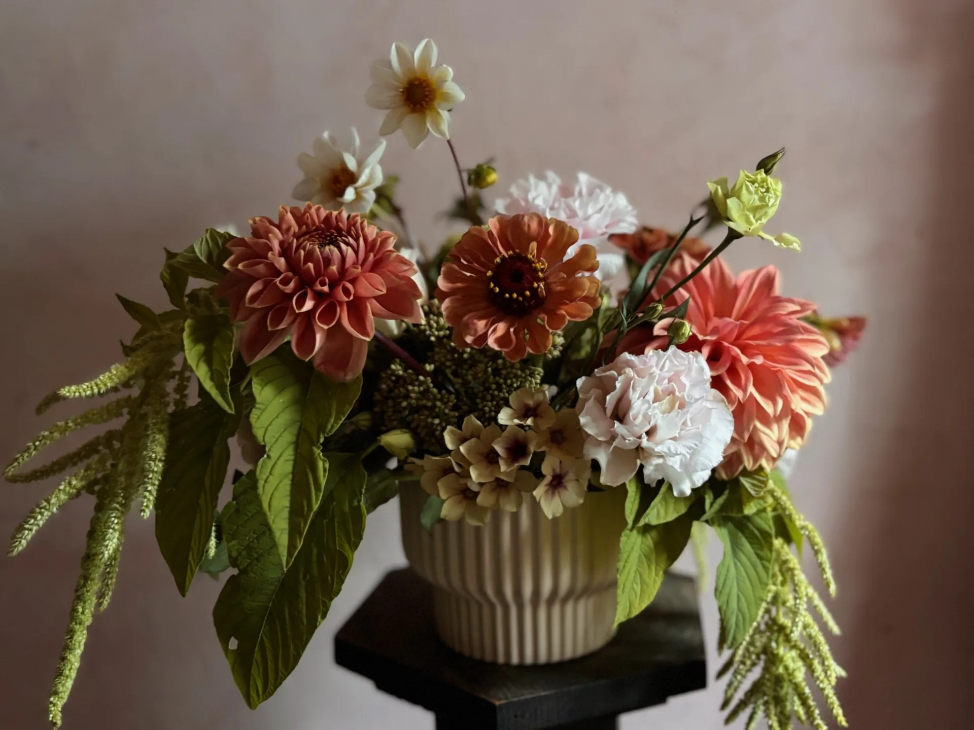 A designer compote arrangement of peach dahlias and seasonal foliage