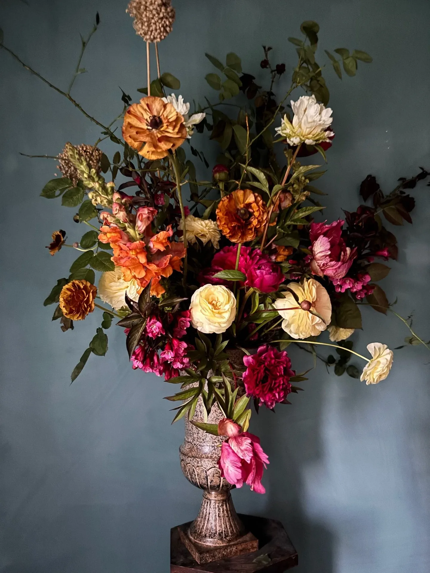 A loose spring arrangement of ranunculus, poppies and foliage in a footed vase by designer Whitney Page