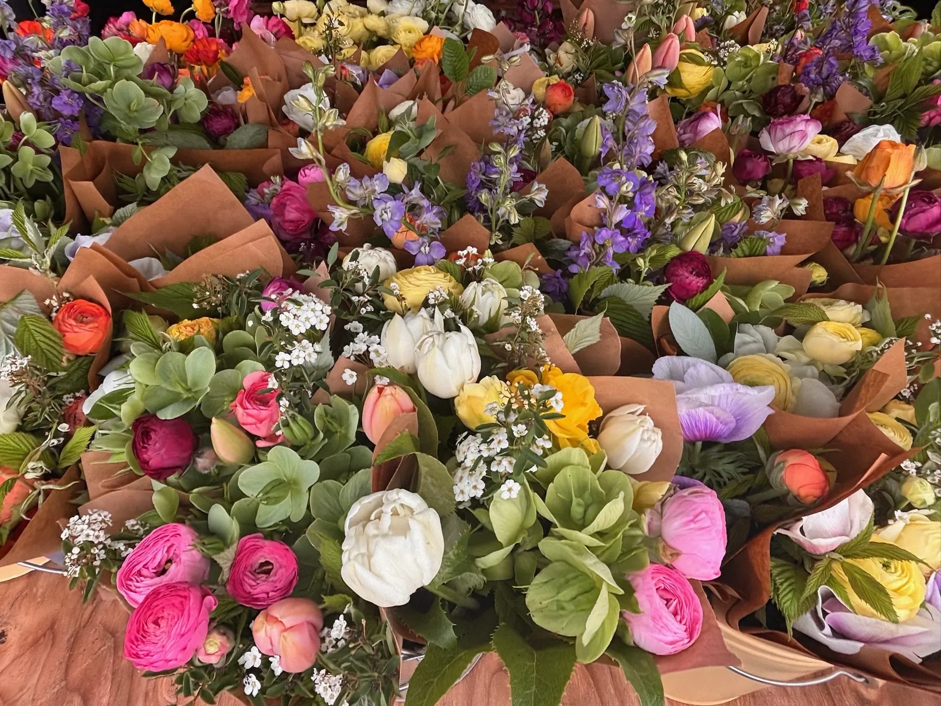 Dozens of wrapped bouquets of ranunculus, sweet peas and tulips