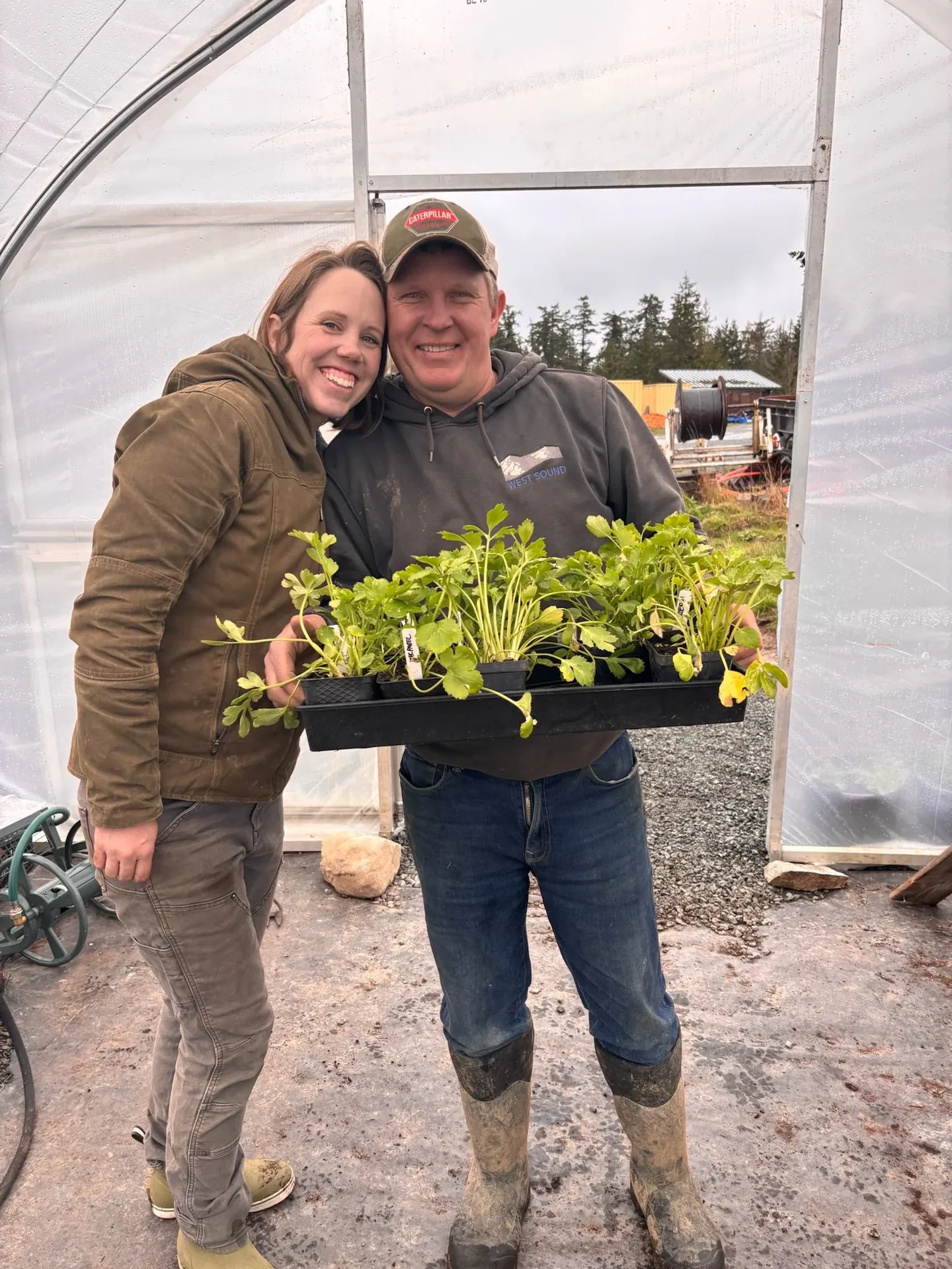 Brian and Laura in the greenhouse holding trays of seedlings