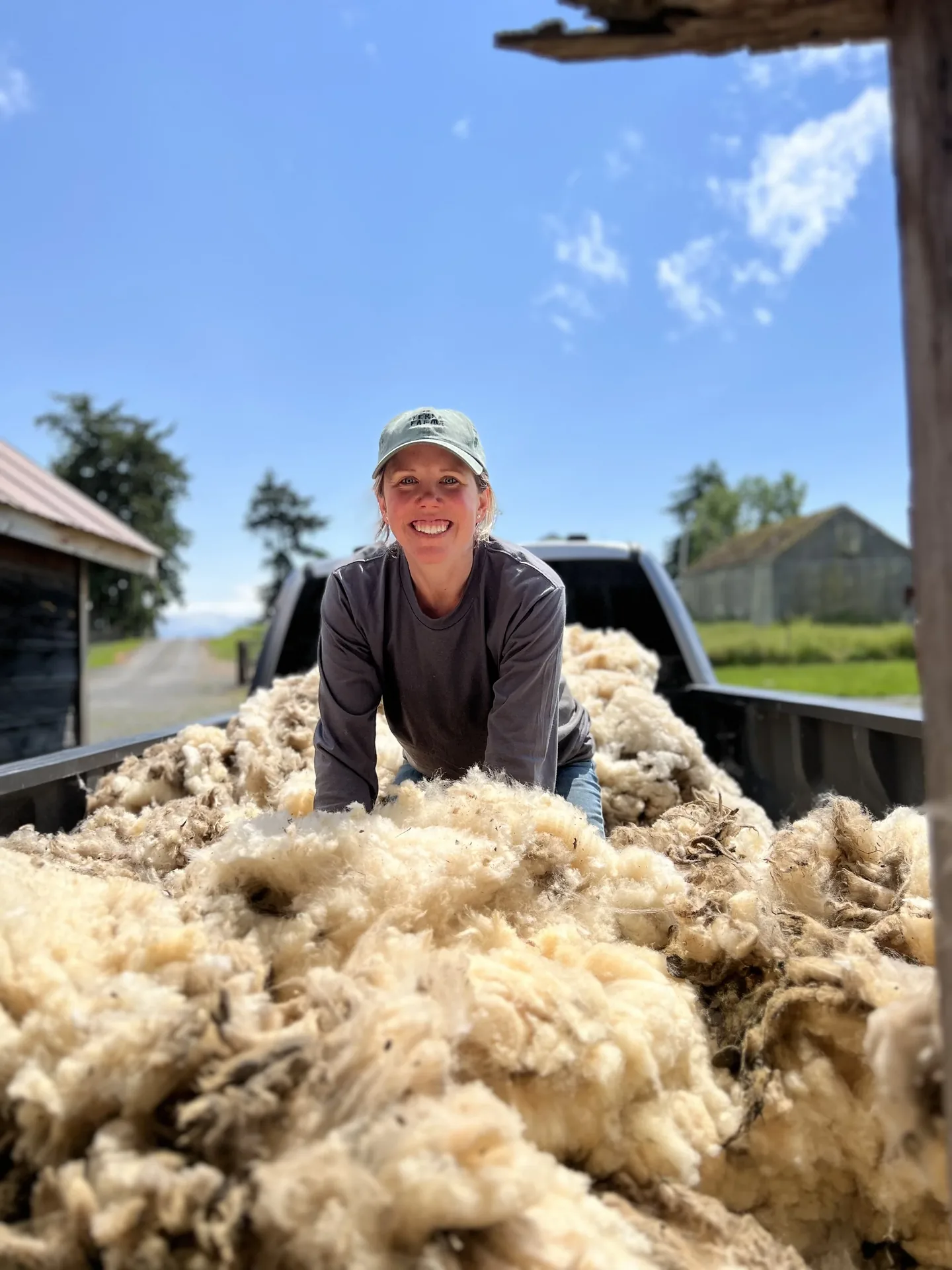 Laura sitting on a bed of freshly shorn wool at a sheep shearing