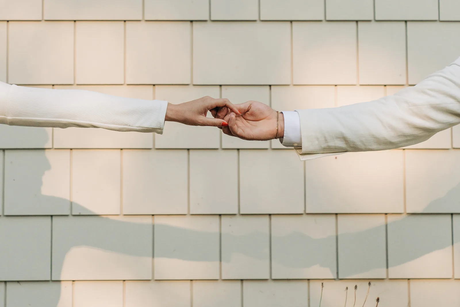Two hands touching gently against a soft brick wall, an intimate moment in romantic lighting