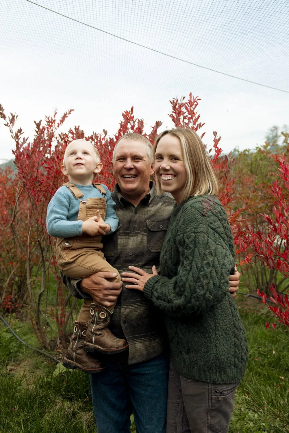 Brian and Laura Torma holding their son among the blueberry bushes in autumn colour