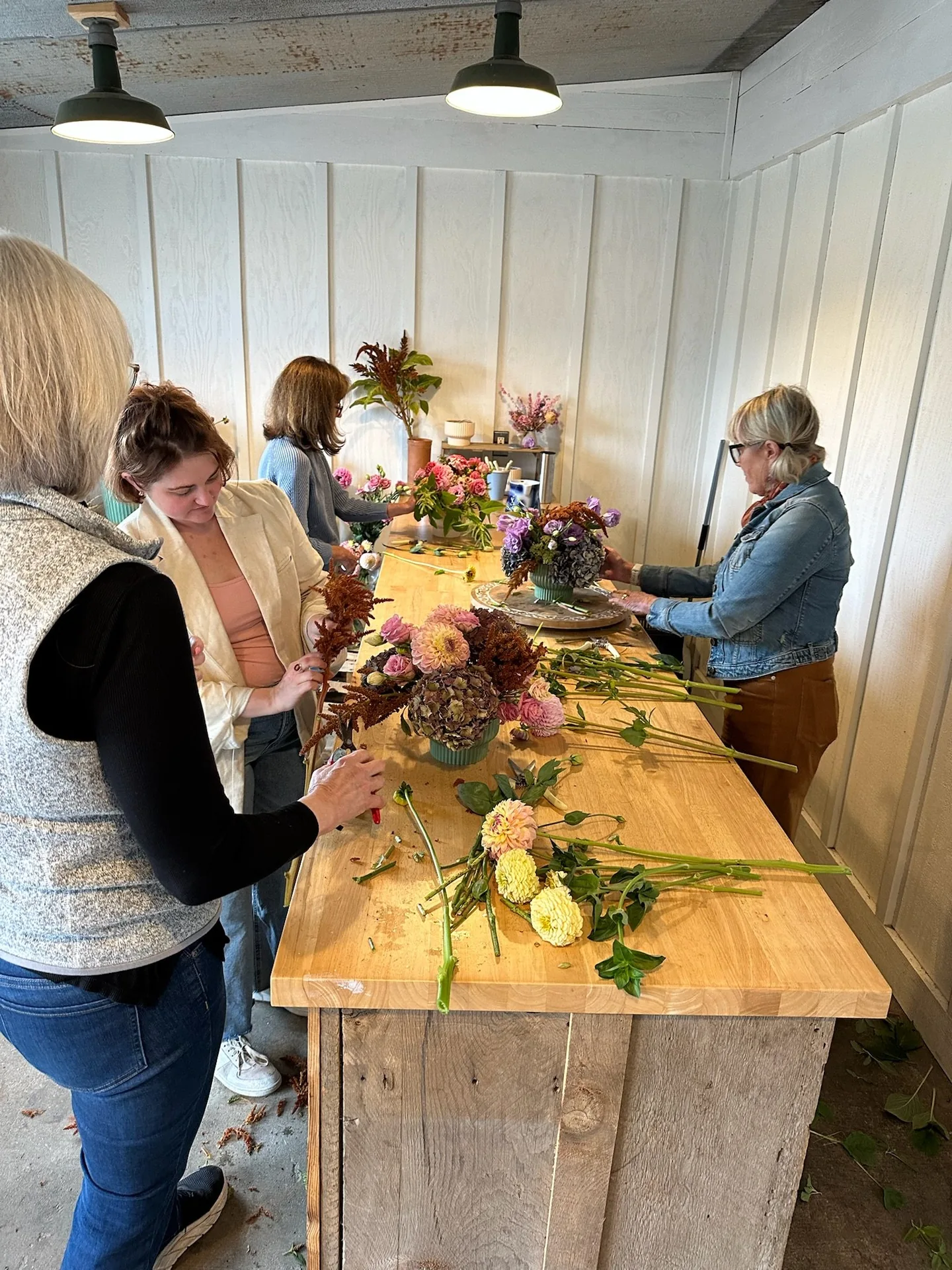Workshop guests arranging dahlias at a long wooden table