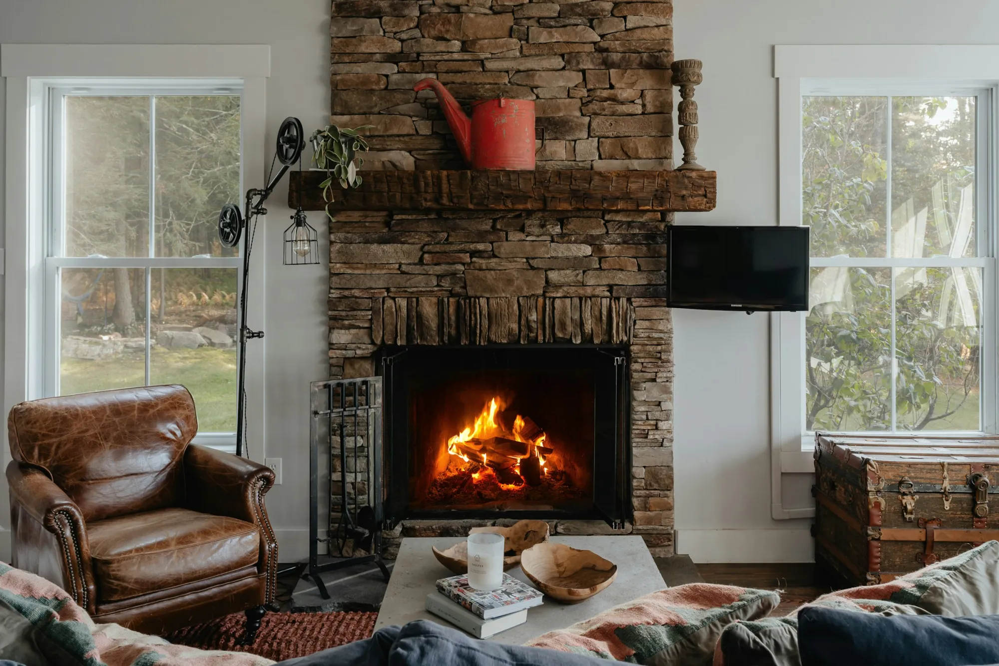 A cozy island living room with a stone fireplace, lit fire, and bright windows.