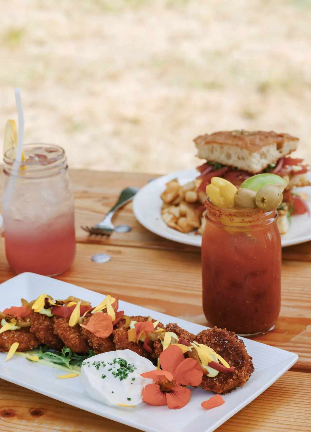 Beautifully plated lunch dishes with fried items garnished with edible flowers, drinks, and sides at Blackfish Café