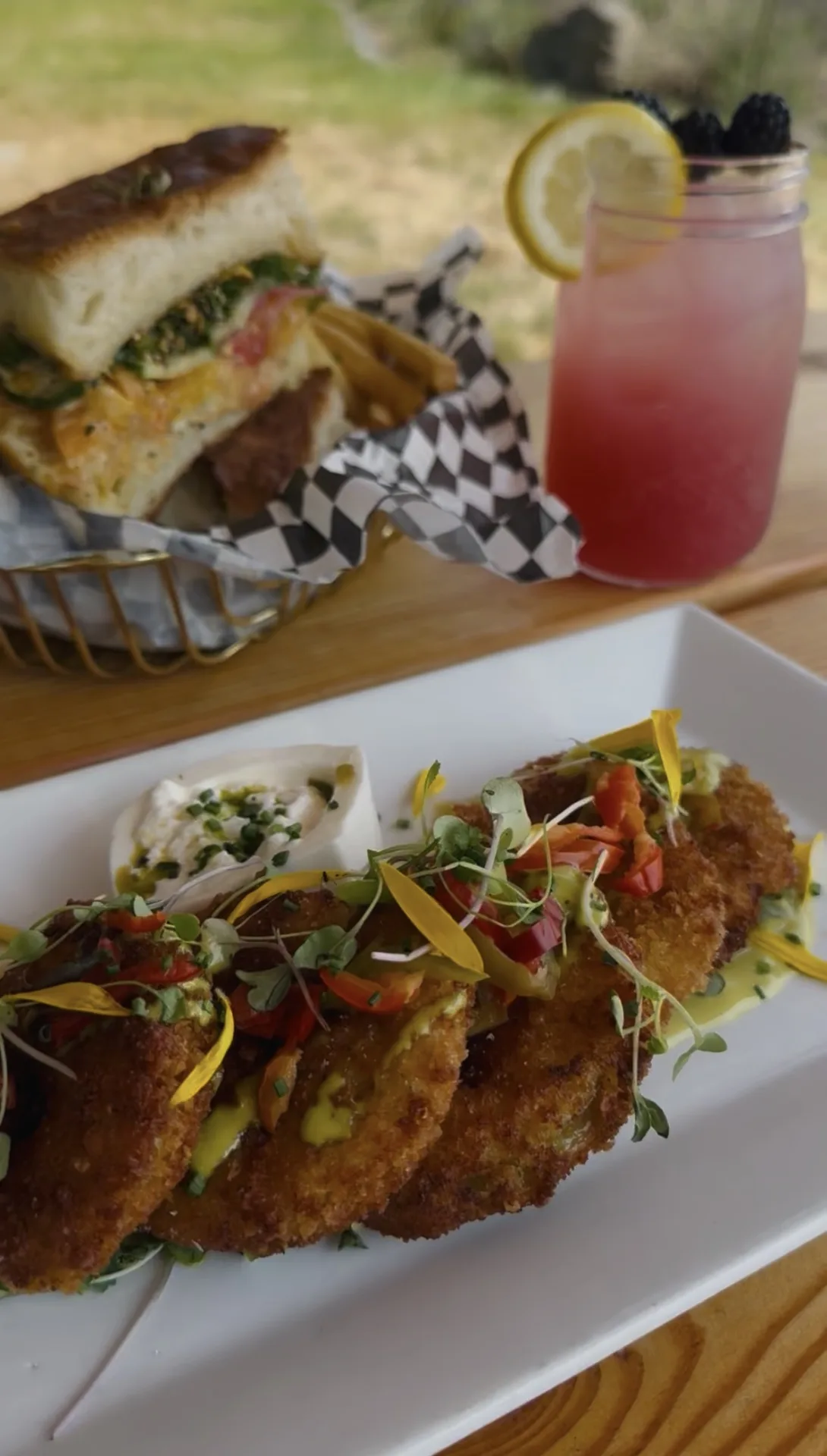 Fried green tomatoes with burrata, a sandwich and fries, and a berry cocktail on The Lawn