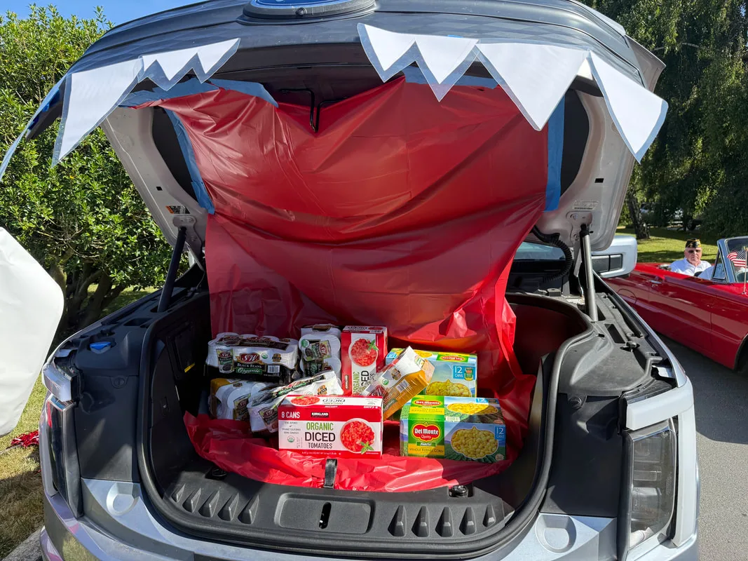 A car trunk decorated as a shark&rsquo;s mouth, filled with donated canned tomatoes, corn and black beans