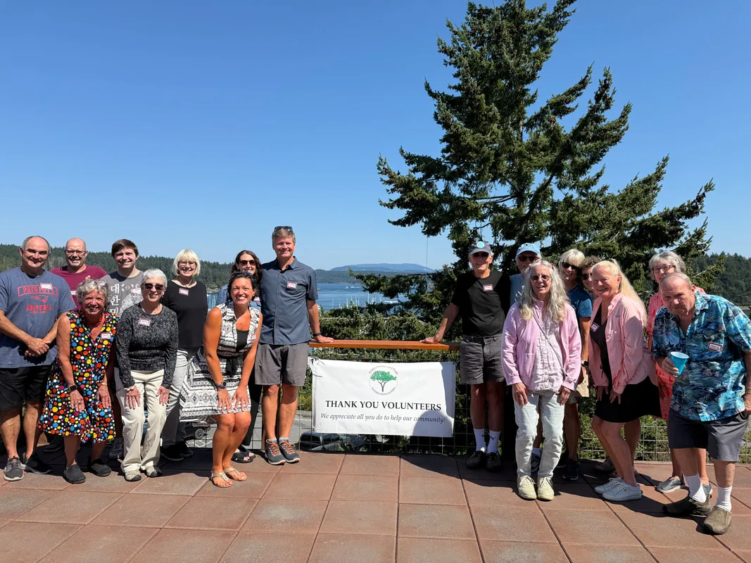 Food bank volunteers gathered on a sunny terrace above Friday Harbor behind a Thank You Volunteers banner